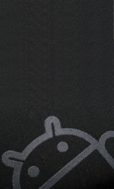 An oversized Android robot sits low in the frame, printed in slightly lighter grey on a woven charcoal cloth so the weave shows through the shape.