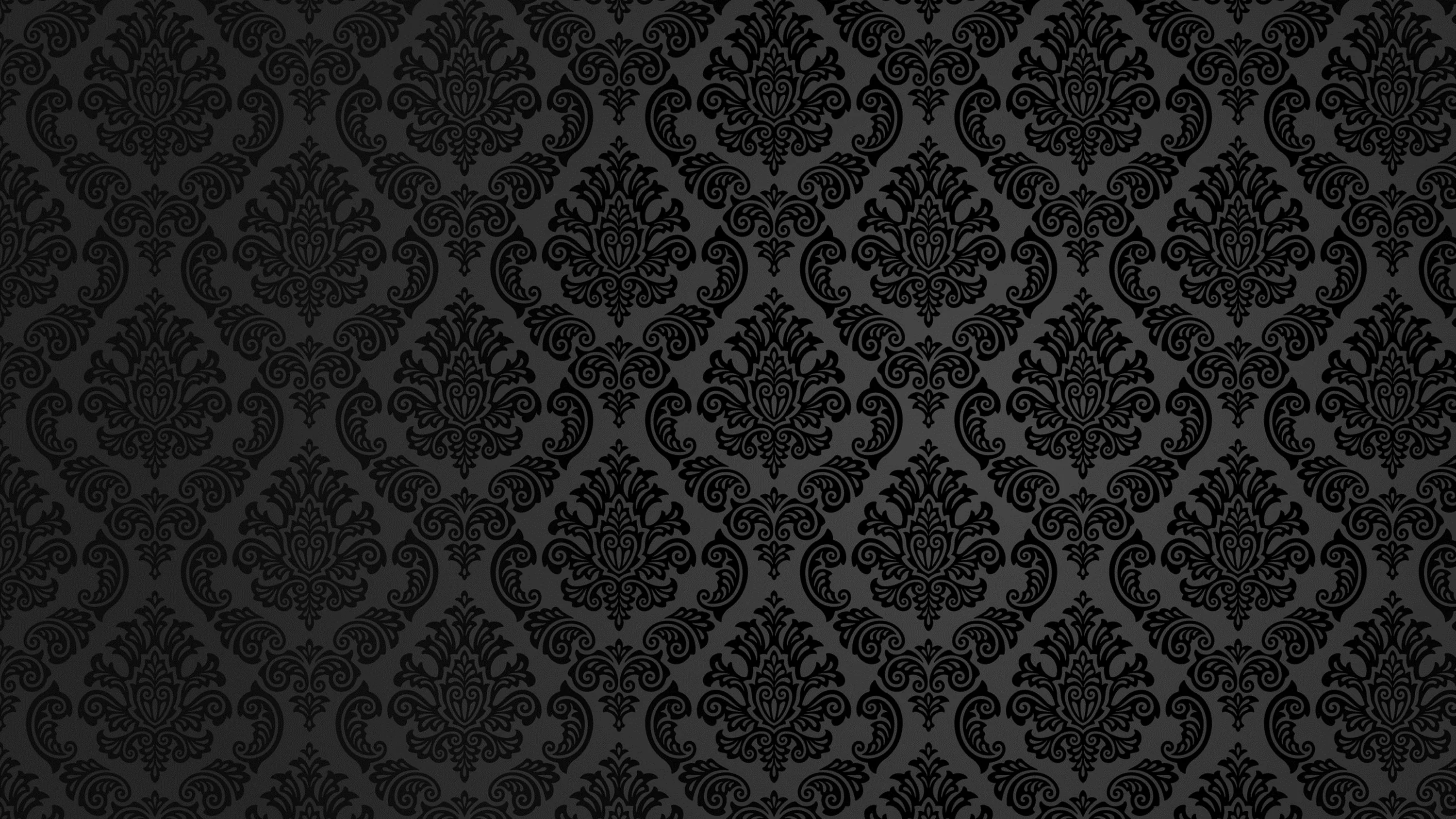 A repeating baroque damask motif pressed into charcoal fabric, the pattern only visible where light grazes the raised edges.
