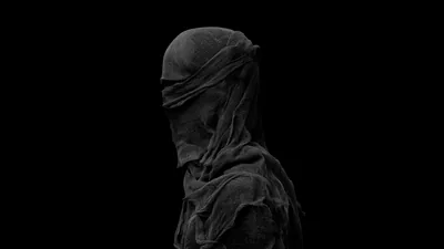 A shrouded figure stands in three-quarter profile, coarse fabric wound over the head and shoulders, everything past the left edge falling to solid black.