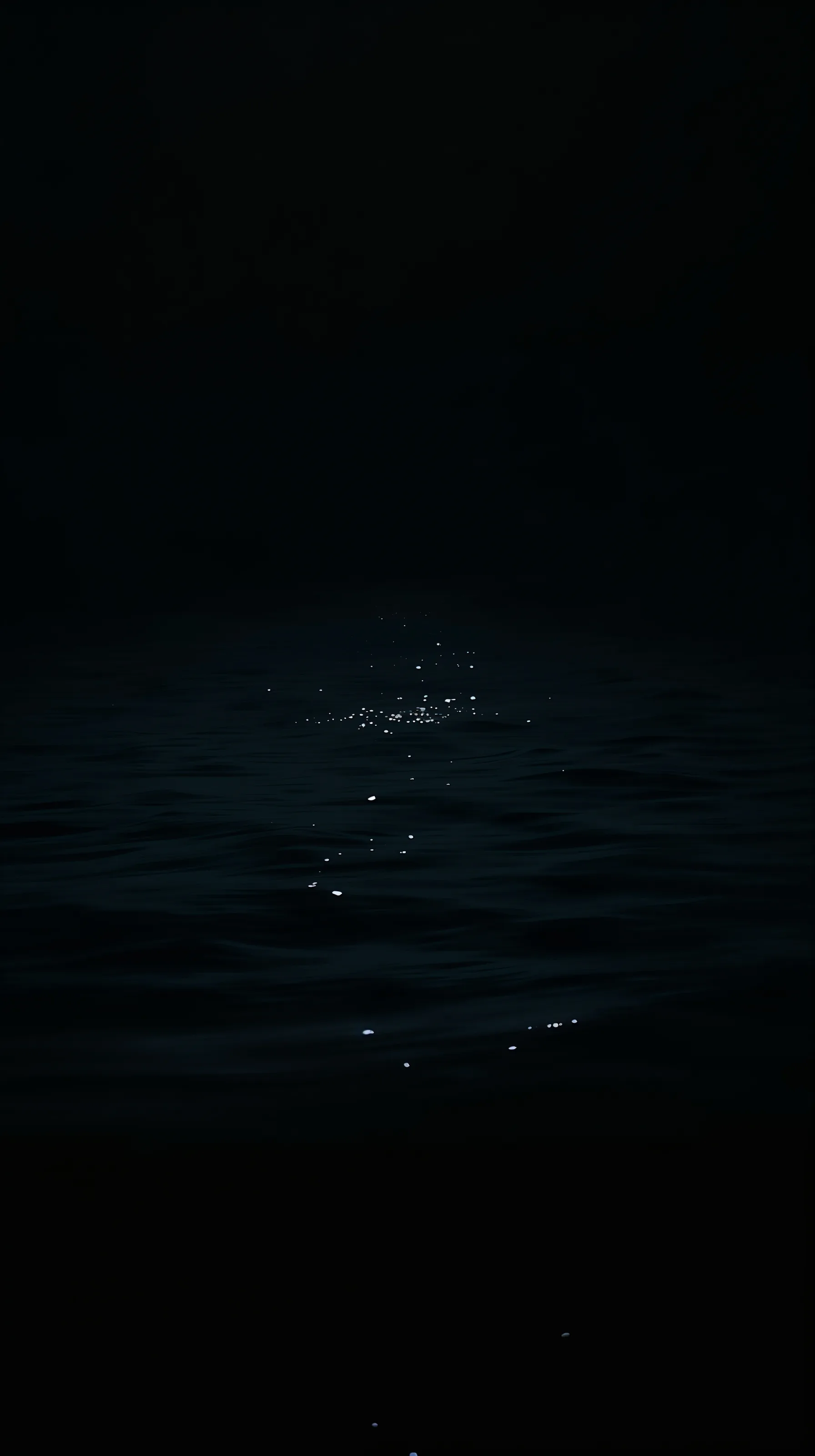 Small points of light break across low swells of dark sea, the horizon lost so the top third of the frame stays empty.