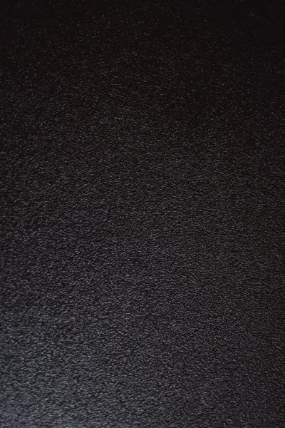 Tightly pebbled black leather filling the frame, the grain sharpest along the left side and softening into shadow at the top corners.
