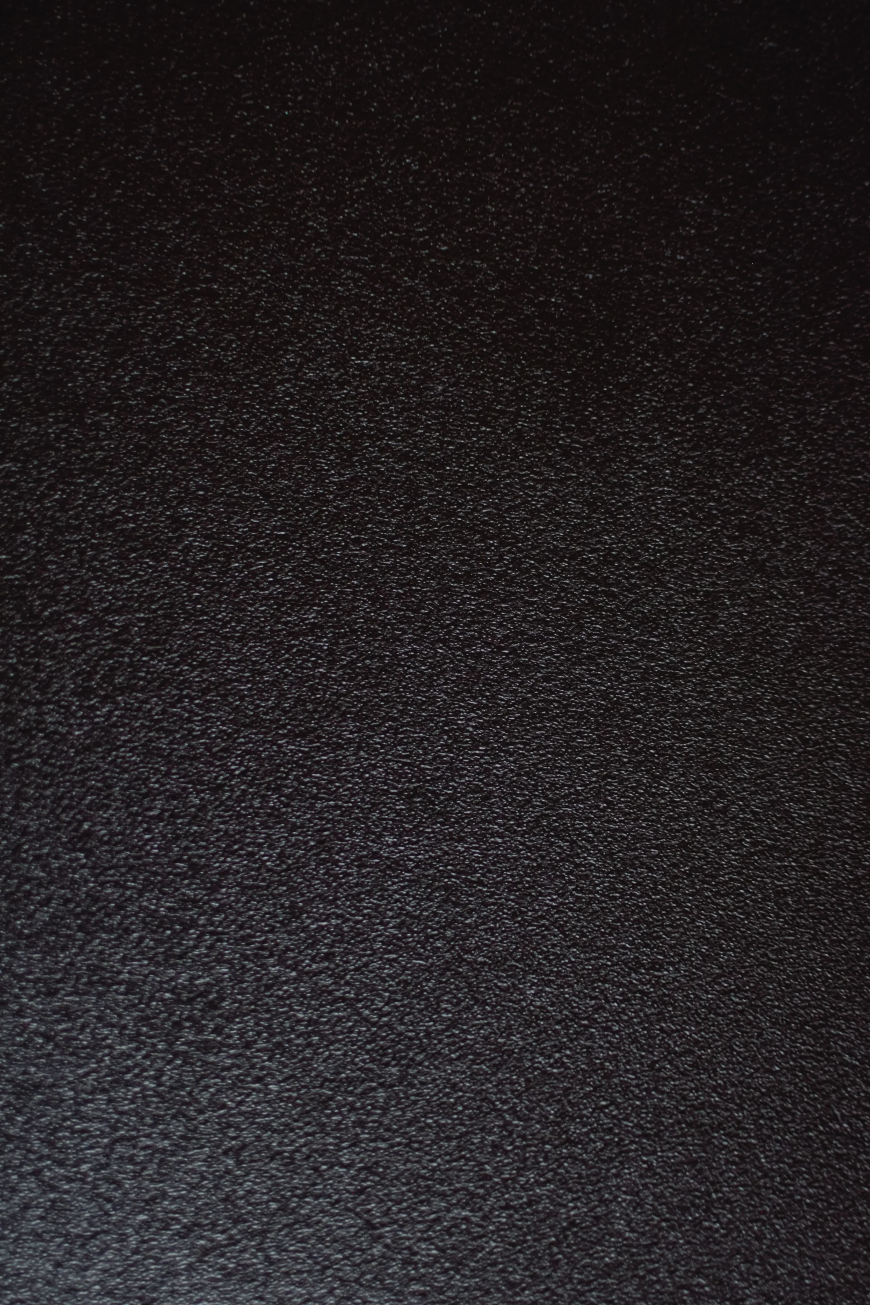 Tightly pebbled black leather filling the frame, the grain sharpest along the left side and softening into shadow at the top corners.