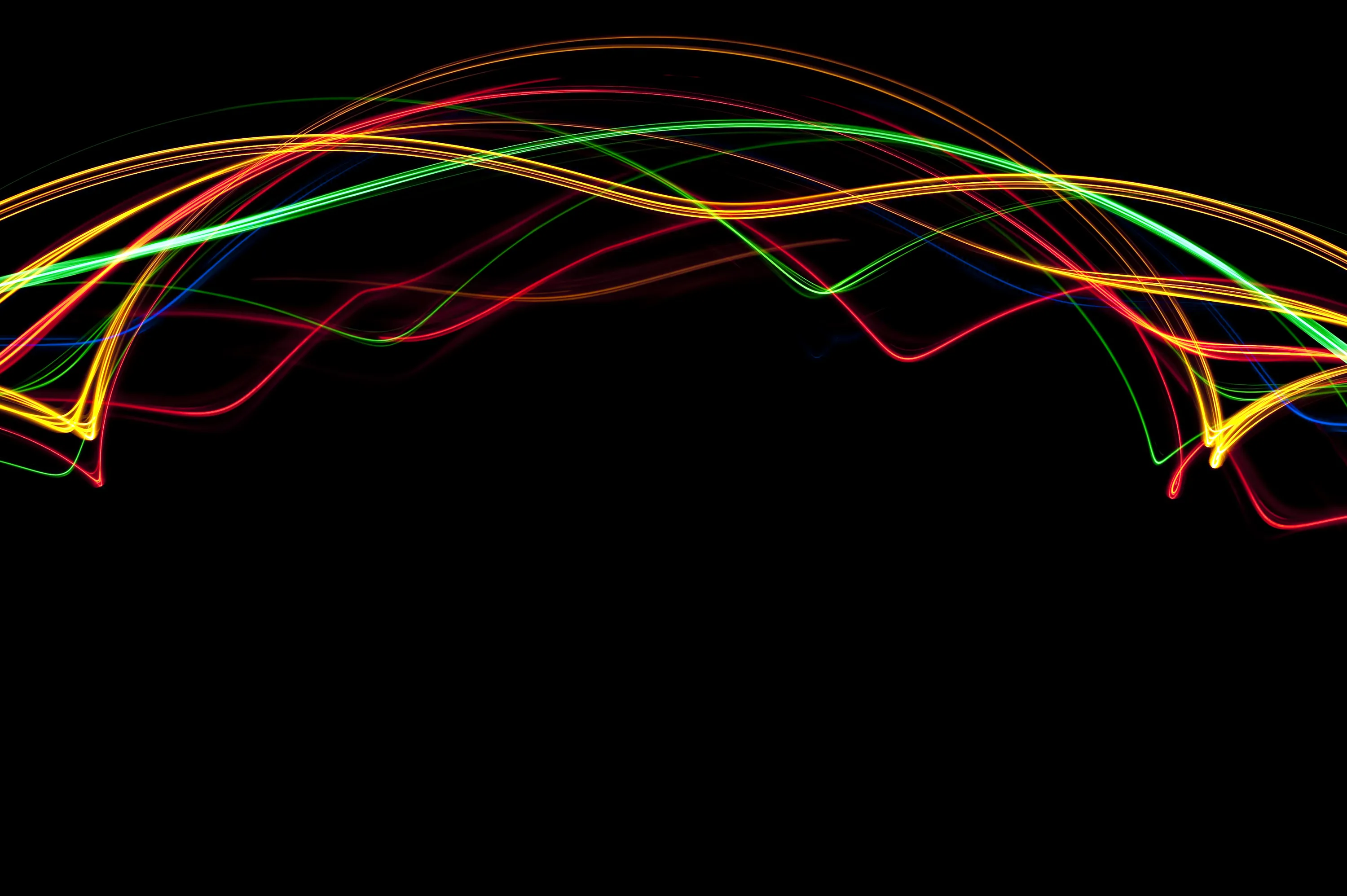Long-exposure trails in red, green and yellow crisscross into an arch across the upper half, the bottom of the frame left completely black.