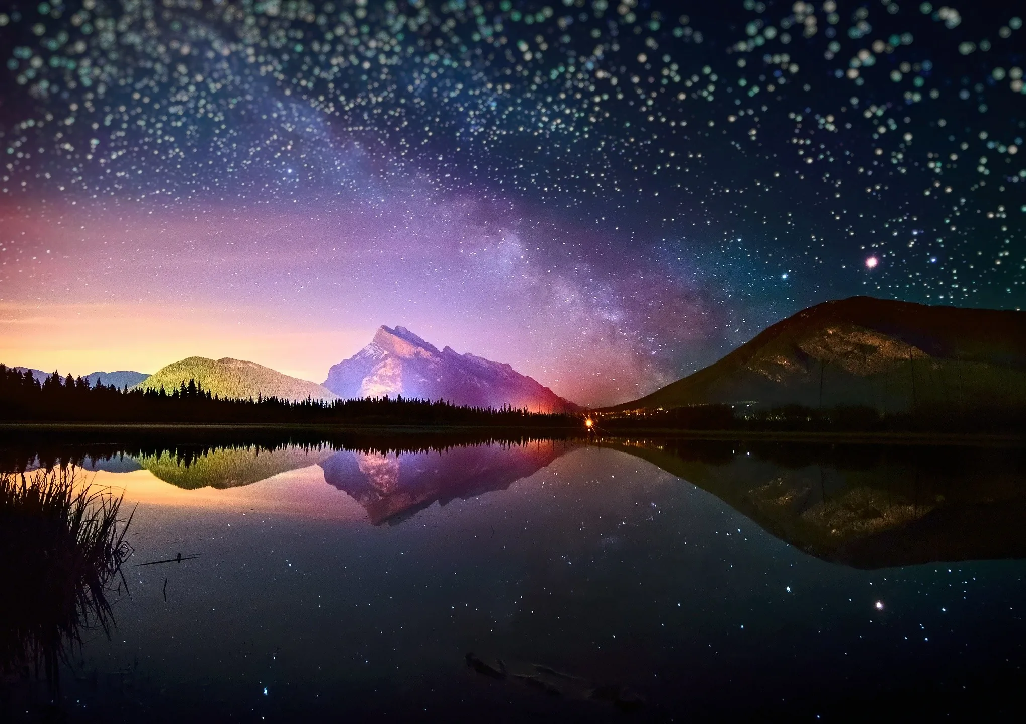 A purple-and-teal starfield doubles in a glassy mountain lake, the mirrored peak sitting dead centre so the image survives a square crop.