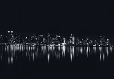 Lit towers stand in a thin band across the middle in monochrome, their reflection breaking up in the water below and black sky above.