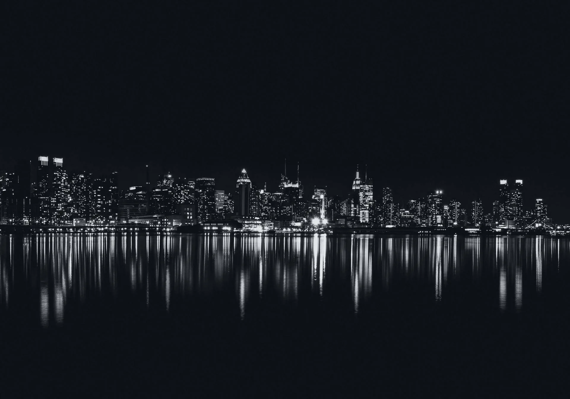 Lit towers stand in a thin band across the middle in monochrome, their reflection breaking up in the water below and black sky above.