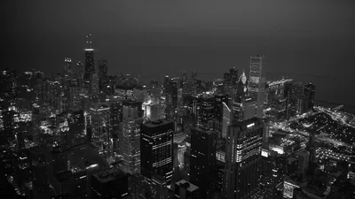A dense grid of towers seen from high up in monochrome, the lake and horizon flat grey behind it.