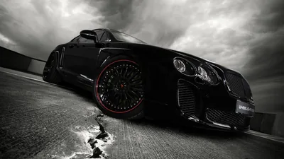 Low angle on a black Bentley with deep red-lipped wheels, heavy grey cloud stacked above the road and a small pool of water catching light near the front tyre.