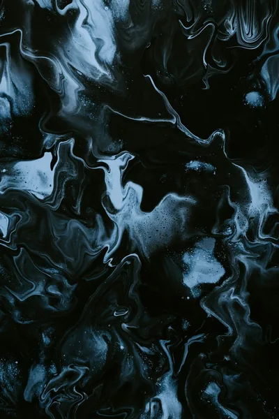 Pale blue ink threads through deep black in a tall frame, the swirls loosening near the top and settling into darker pools at the base.