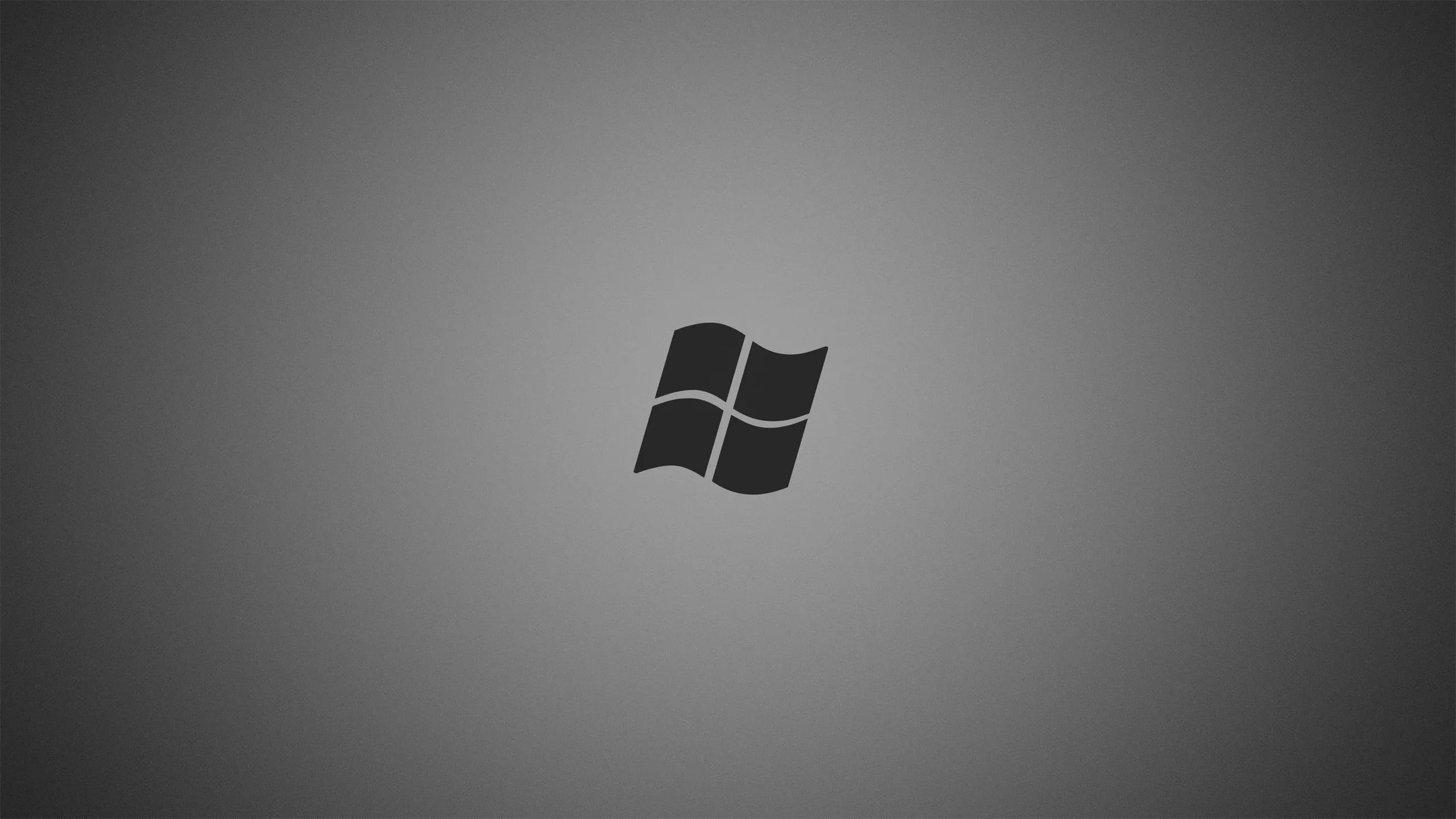 The four-pane Windows flag sits small and dark at the centre of a soft grey radial gradient, edges dimming toward the corners.