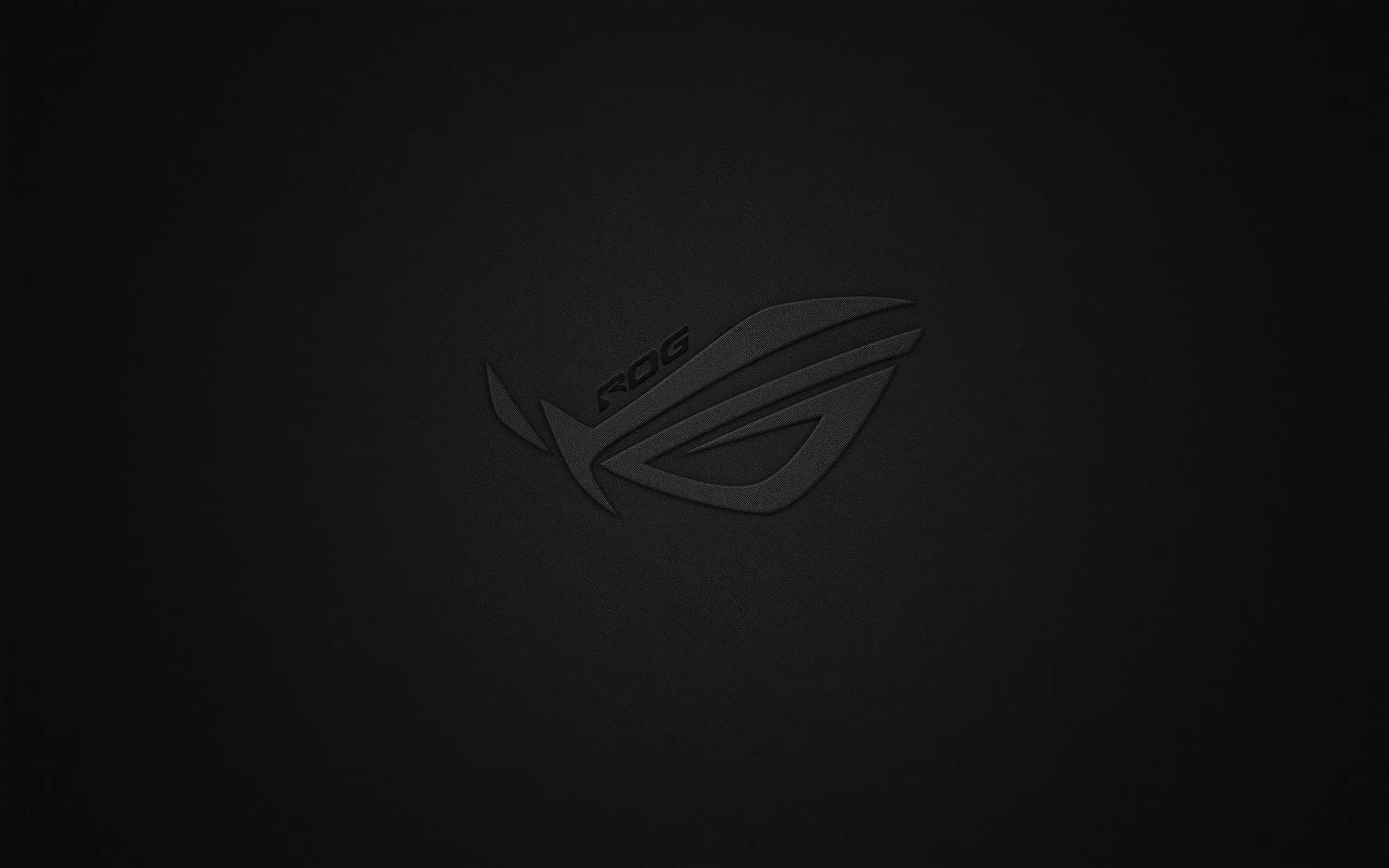 The ROG eye sits centre-frame only a shade lighter than the near-black ground, so the logo all but disappears until the screen brightens.