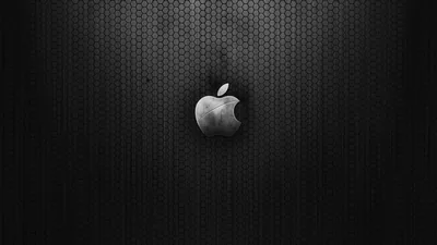 The chrome Apple mark sits at the centre of a dark honeycomb mesh panel, monochrome with a faint spotlight behind it.
