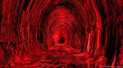 A rough-hewn rock tunnel recedes to a black vanishing point, the arch and floor drenched in a single red light source.