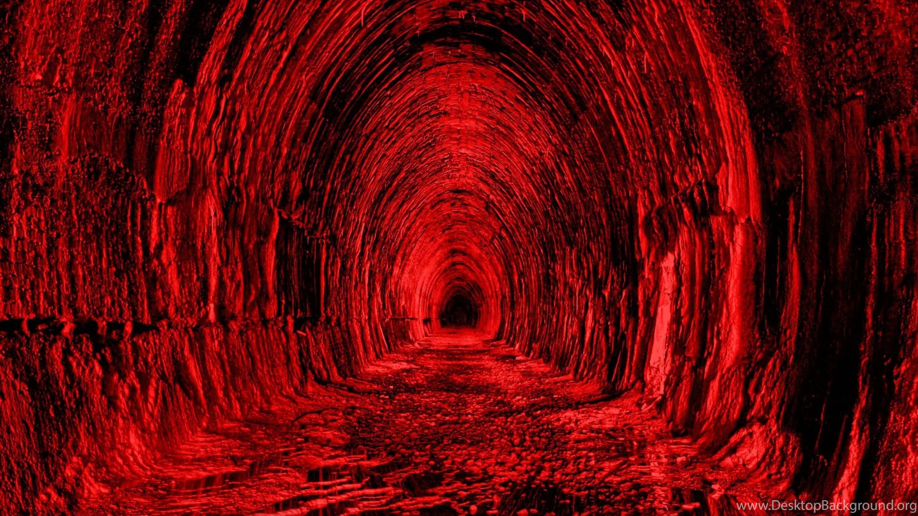 A rough-hewn rock tunnel recedes to a black vanishing point, the arch and floor drenched in a single red light source.