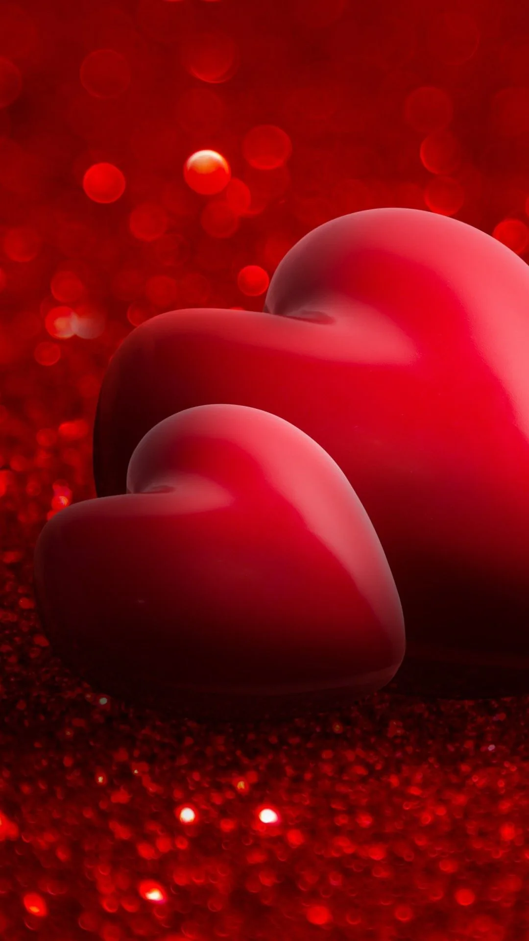Two smooth three-dimensional hearts sit on a bed of red glitter, highlights sliding along their curves and the background dissolving into sparkle.