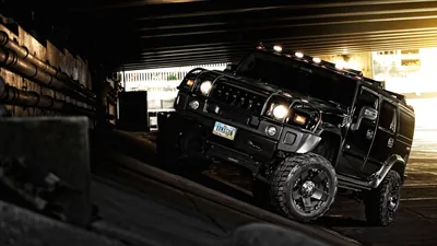 The big SUV turns through a dim underpass on chunky off-road tyres, roof-mounted light bar dark and a bare concrete wall running along the left.