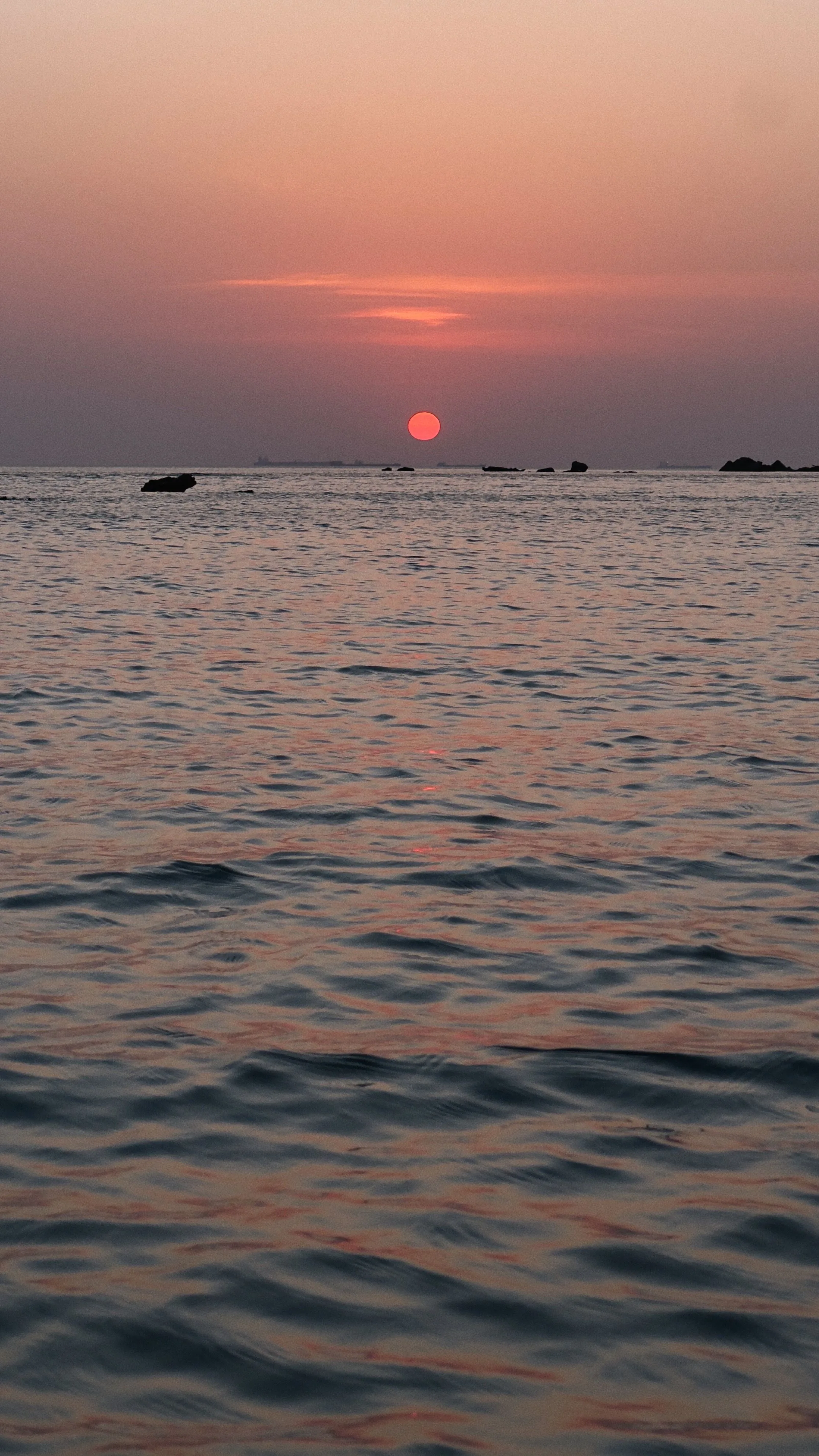 A small hazy sun sits over slow-rolling water in muted pink and grey; most of the frame is soft, even texture that keeps app icons readable.