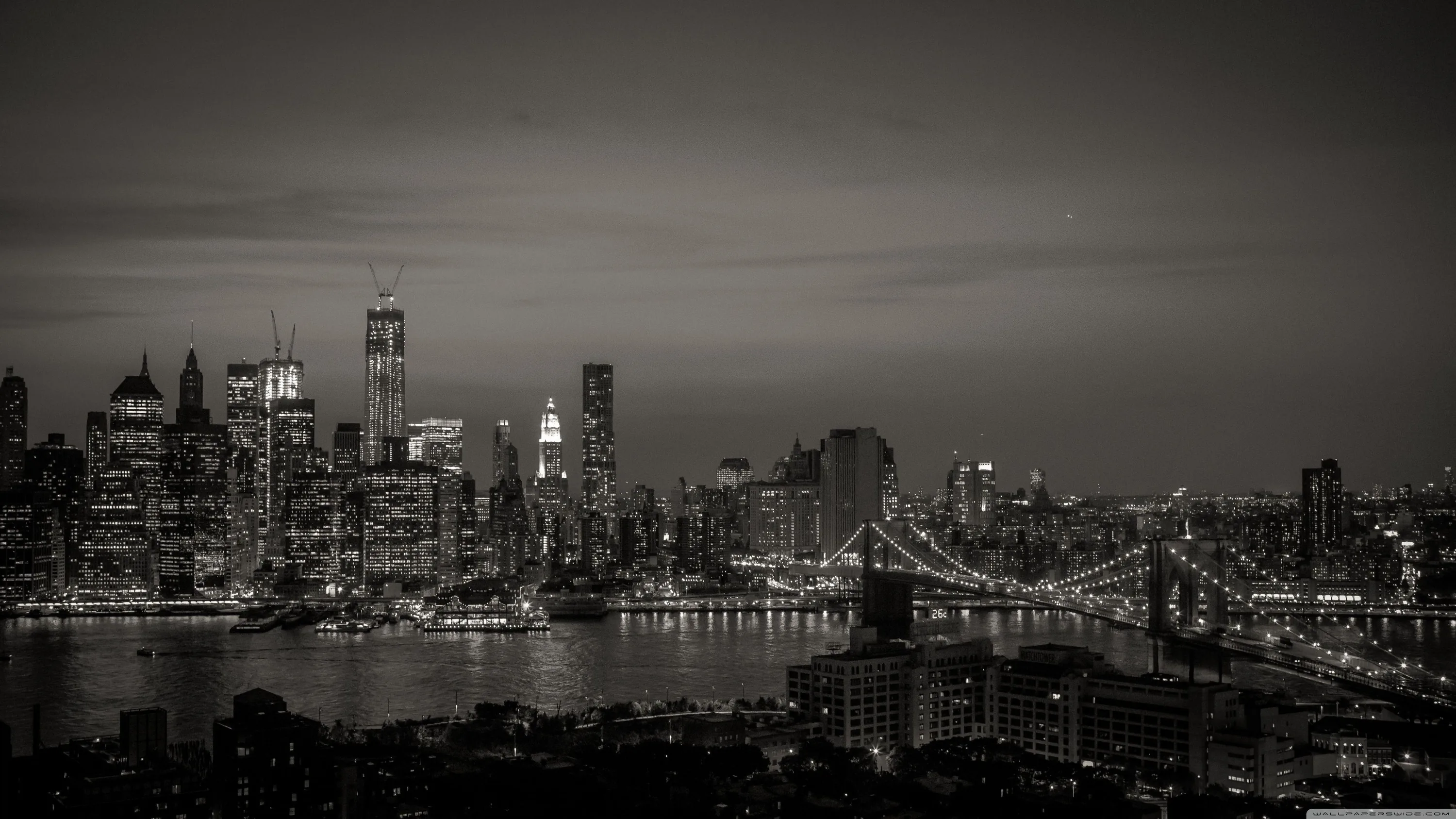 A whole skyline and suspension bridge sit under a heavy sky, the water black and the lights spread thin along the shore.