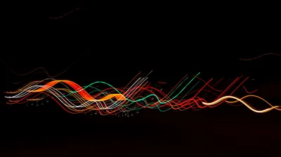 Long-exposure light painting leaves red, green and amber ribbons swaying across an otherwise empty black frame.