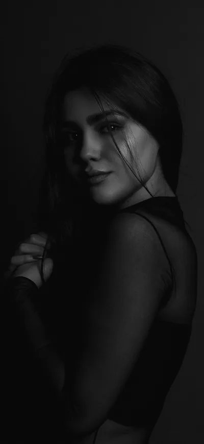 A figure turns toward the camera in near-darkness, light catching the face and shoulder while the rest falls away.