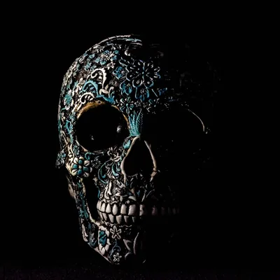 A skull covered in ornate carved filigree, turquoise inlay catching the light along the brow and cheekbone while the rest sinks into shadow.
