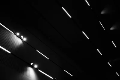 Rows of white tube lights run diagonally across a black ceiling in monochrome, most of the frame staying deep black between the fixtures.