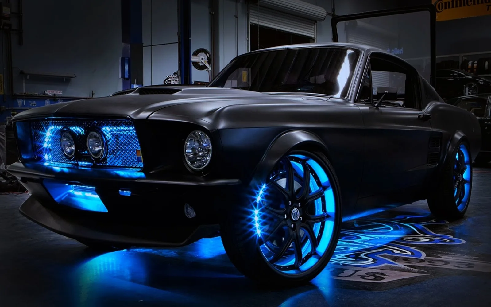 A custom fastback Mustang in a workshop, blue LEDs ringing the wheels and spilling across the floor under the sills.