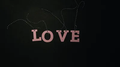 Wooden letters spelling love hang from a thin beaded string against a near-black wall, the top third left empty for icons.