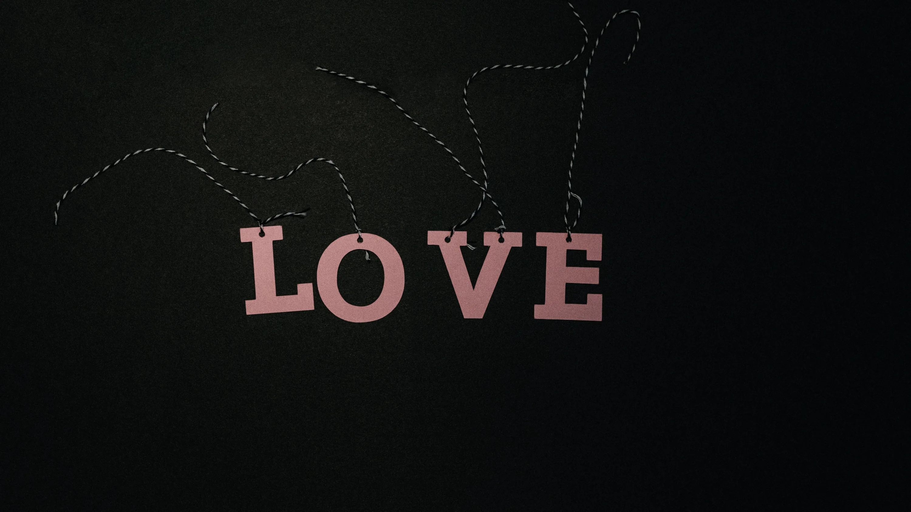 Wooden letters spelling love hang from a thin beaded string against a near-black wall, the top third left empty for icons.