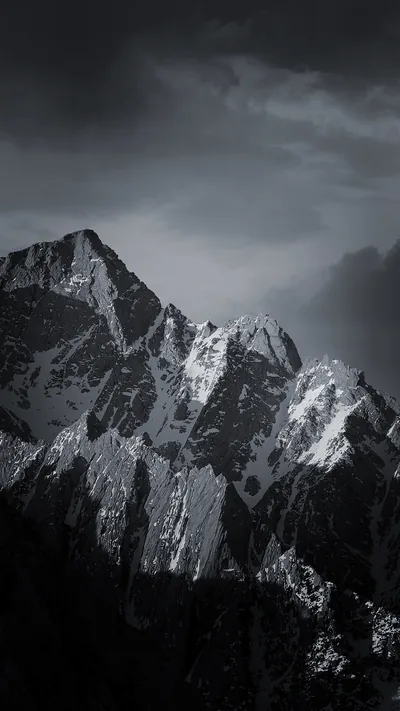 A snow-streaked peak fills the lower half in hard grey, heavy cloud dragging across the summit and the rock face falling into shadow on the right.