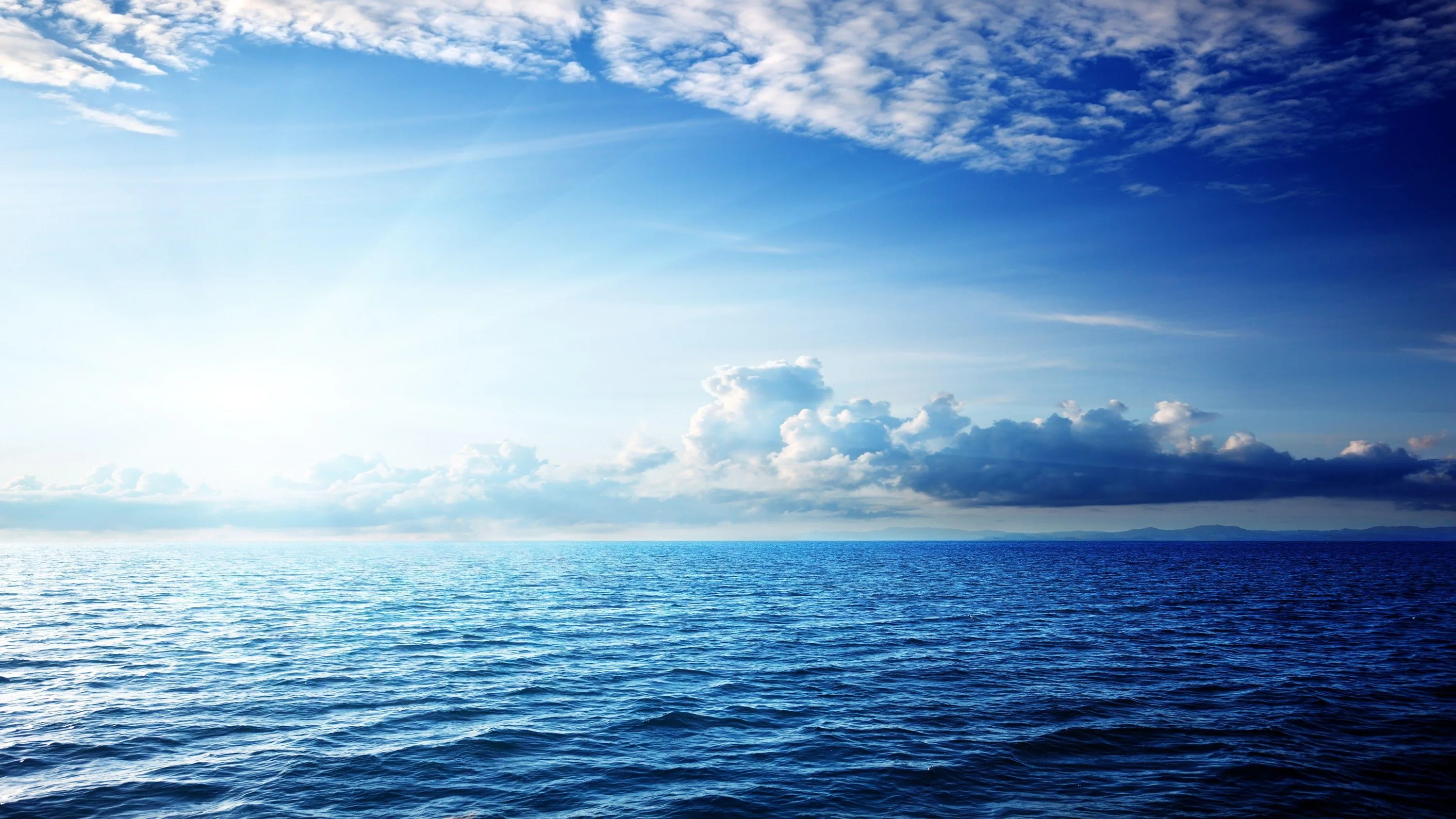 Gentle ripples texture a deep blue sea below wispy clouds, the horizon sitting dead centre so the crop works on almost any screen.