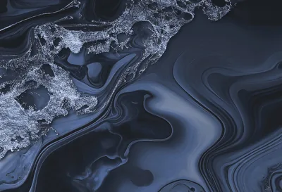 A crust of silvery froth spills across the upper left while glossy slate ink folds sweep toward the right, ridged like sand under shallow water.