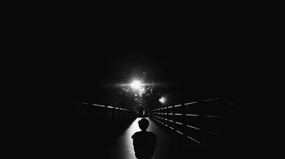 One flaring lamp burns at the centre of this black and white bridge scene, the round silhouette of a head rising at the bottom edge of the frame.
