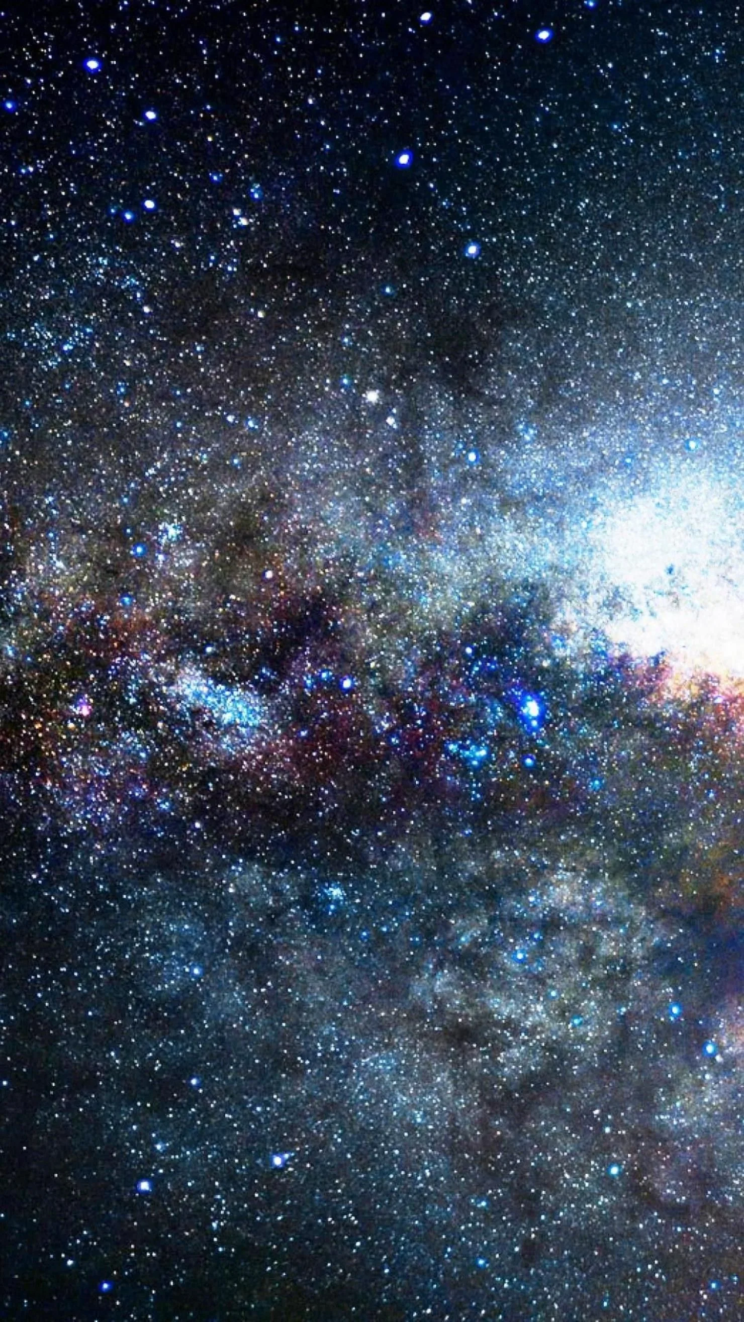 Thousands of stars crowd the galactic core, dust lanes threading dark gaps through a glow that brightens toward the upper right of the frame.