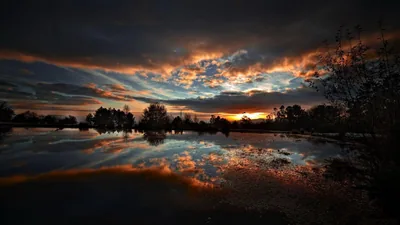 Orange light burns through a broken cloud bank and repeats exactly in the flooded field below.