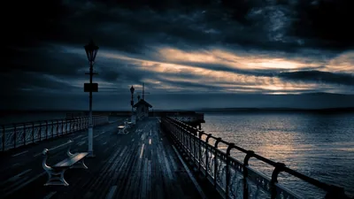 A pier with iron railings runs out toward the sea, storm cloud breaking over the water at the horizon.