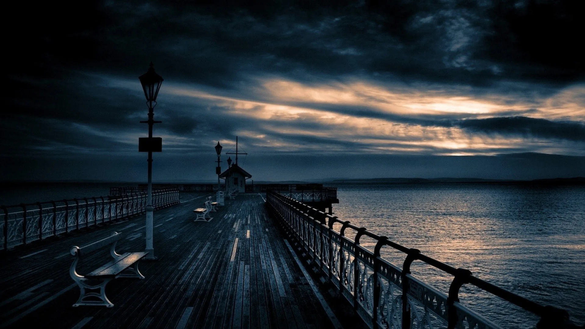 A pier with iron railings runs out toward the sea, storm cloud breaking over the water at the horizon.