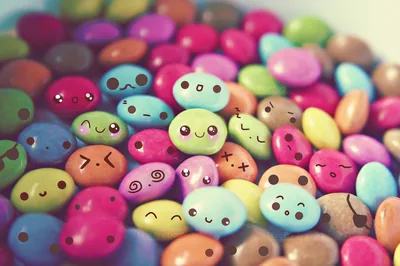 A macro photo of sugar coated chocolate buttons, each inked with a different expression; the shallow focus blurs the top rows into soft colour.