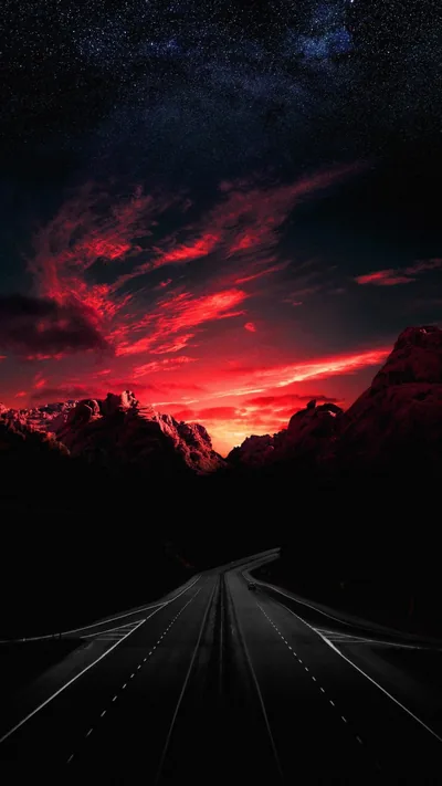 Red-lit clouds burn across the middle of the frame while the road's lane markings pull toward the horizon; the starry top third stays dark enough for a clock.