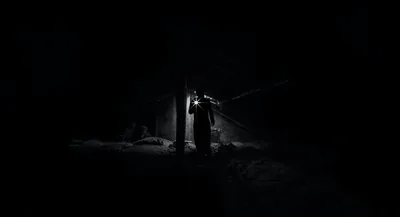 A lone silhouette stands in a shaft of weak light inside a crumbling structure, everything else in shadow.