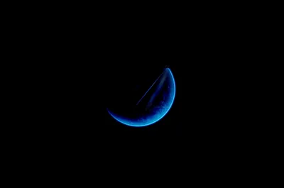 A crescent rim glows electric blue out of total darkness, tilted low-left of centre — everything beyond the arc is true black for OLED screens.