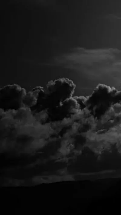Heavy cumulus clouds stack across a near-black sky, the ridge of a hill cutting a flat dark line along the bottom of the frame.