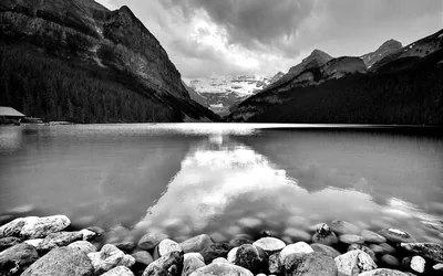 Rounded stones fill the foreground and lead the eye across still water to a glacier valley, clouds sitting low between the ridges.