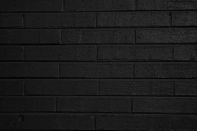 Long thin bricks painted flat black run in even rows, the paint thick enough to soften the mortar lines and dull most of the light.