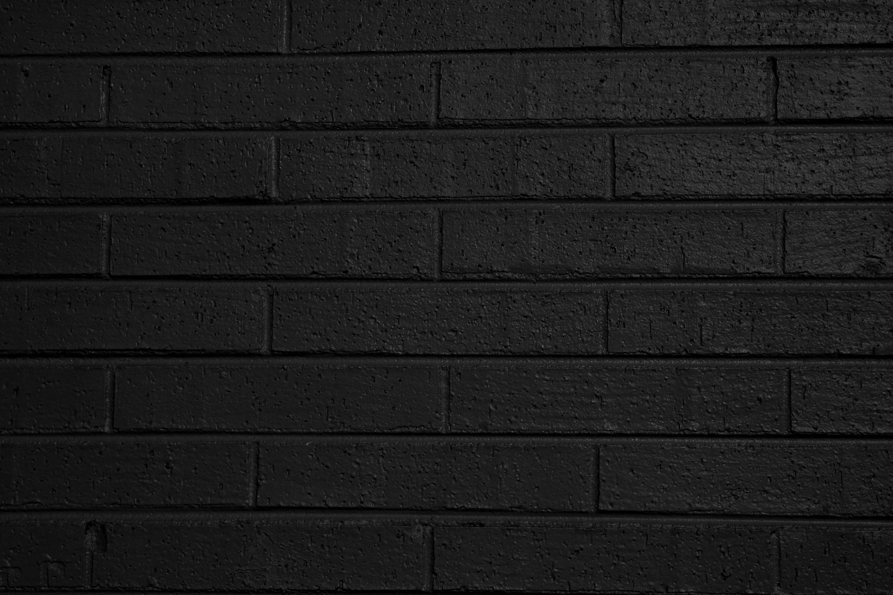 Long thin bricks painted flat black run in even rows, the paint thick enough to soften the mortar lines and dull most of the light.