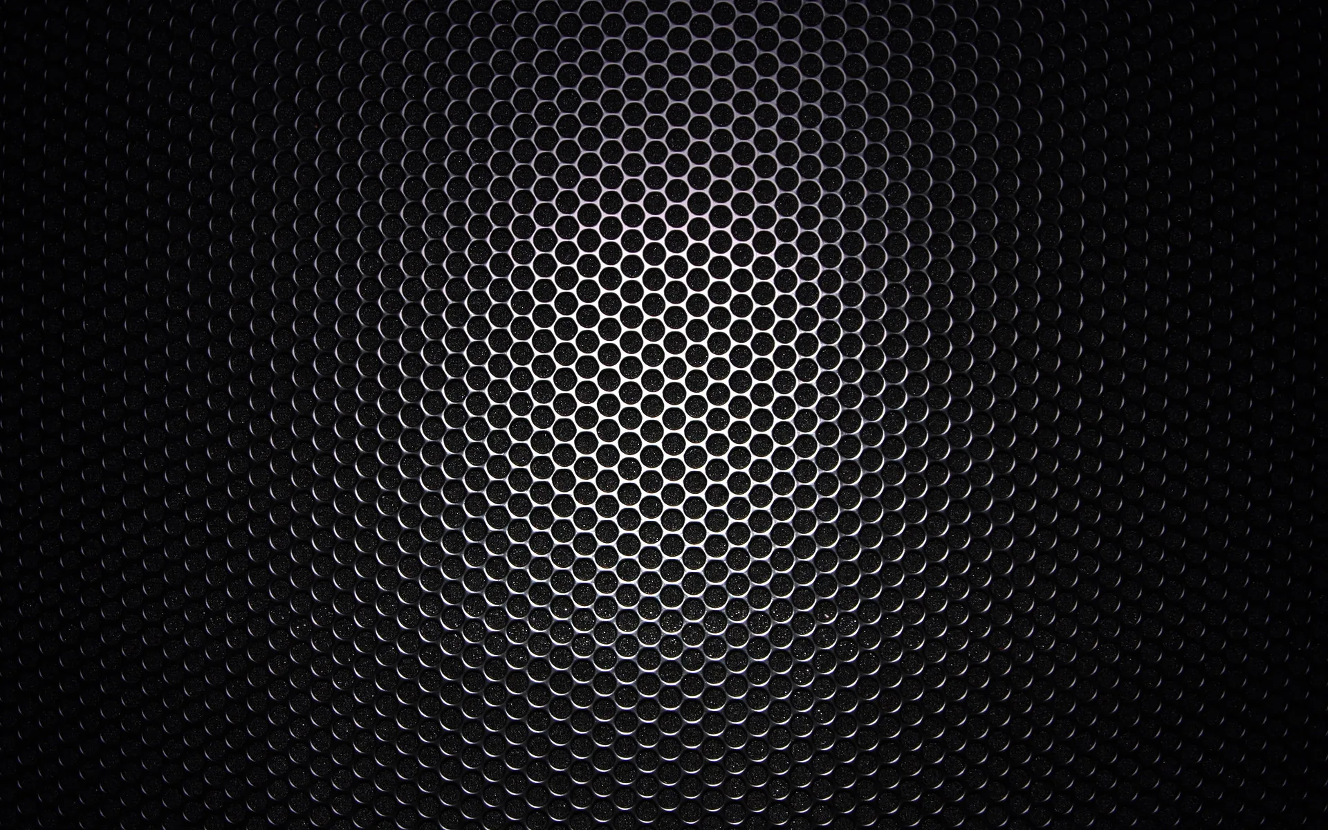 A honeycomb metal grille curves away from the viewer, the mesh catching light along the top and dissolving into black at the sides.
