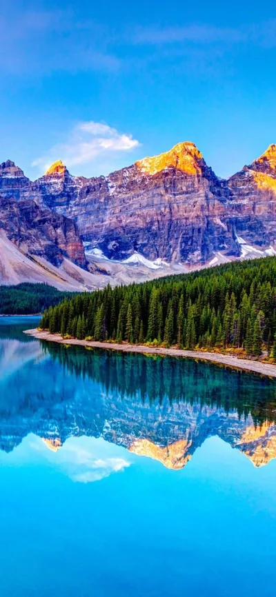 Sunlit rocky peaks and a pine shoreline mirror in flat turquoise water, the clear blue sky keeping the top of the frame simple for a clock.