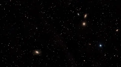 Half a dozen small galaxies sit at different angles across a near-black sky, faint brown dust drifting between widely spaced stars.