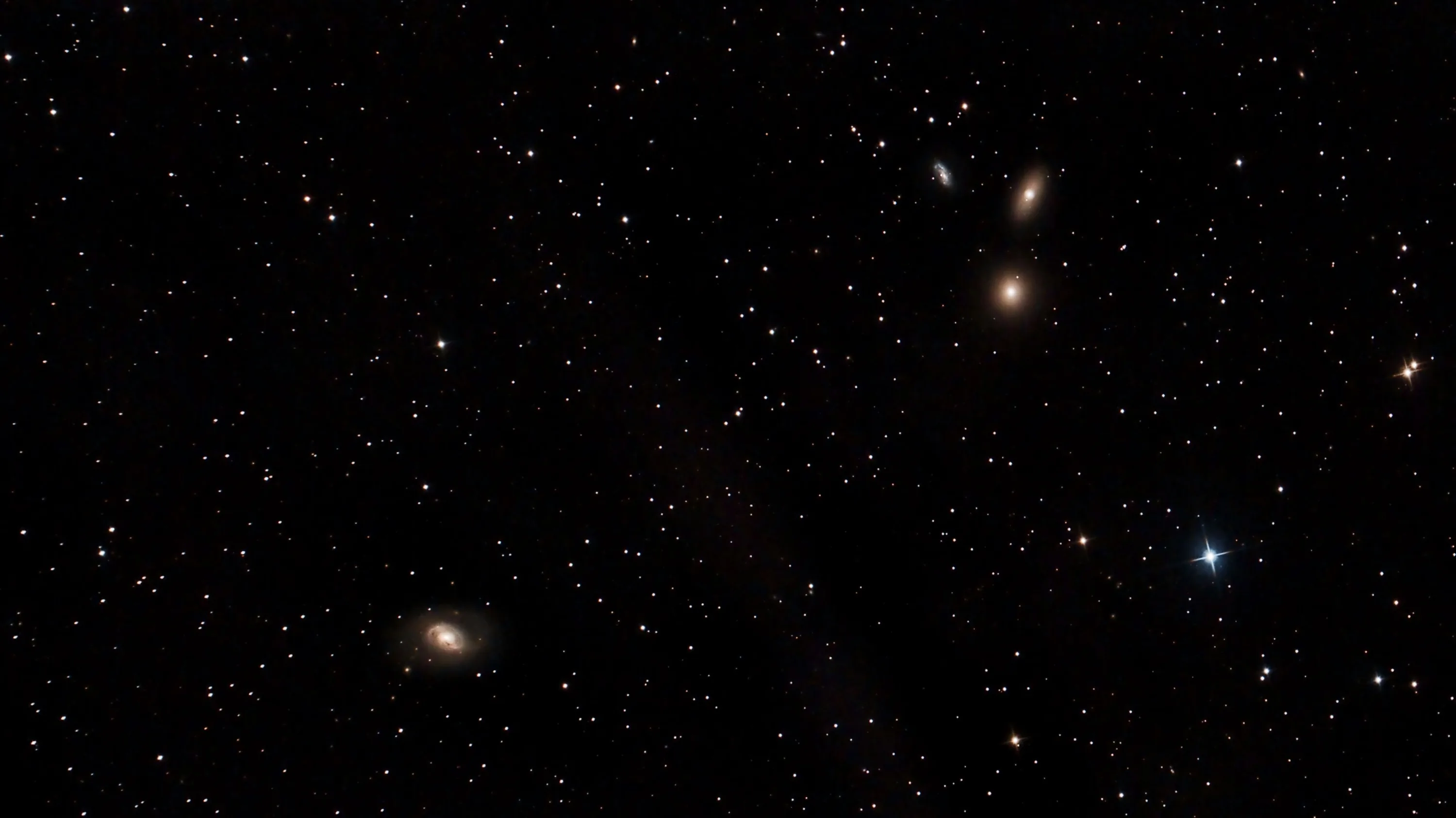 Half a dozen small galaxies sit at different angles across a near-black sky, faint brown dust drifting between widely spaced stars.