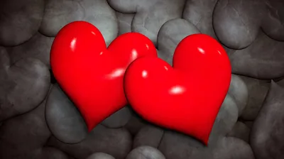 Two rendered red hearts overlap on a bed of smooth grey pebbles, highlights along their tops picking up a soft studio light.